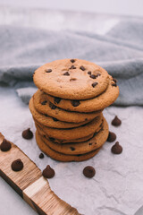 chocolate chip cookies on light background with linen napkins, a wooden cutting board, and baking paper. Yummy food background. Dessert image.