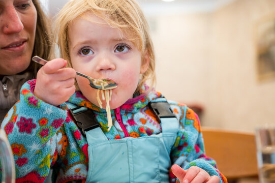 Cute blonde girl eating beef noodle soup in a restaurant with her mother.