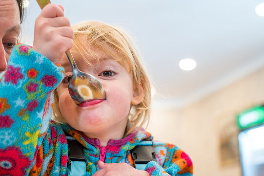 Cute blonde girl eating beef noodle soup in a restaurant with her mother.
