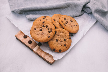 chocolate chip cookies on light background with linen napkins, a wooden cutting board, and baking paper. Yummy food background. Dessert image.