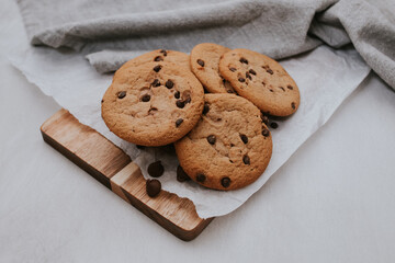 chocolate chip cookies on light background with linen napkins, a wooden cutting board, and baking paper. Yummy food background. Dessert image.