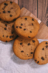 Chocolate chip cookies with baking paper on wooden background. Freshly baked sweets.