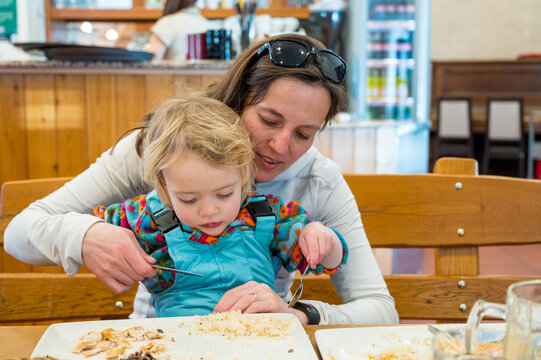 Cute blonde girl eating beef noodle soup in a restaurant with her mother.