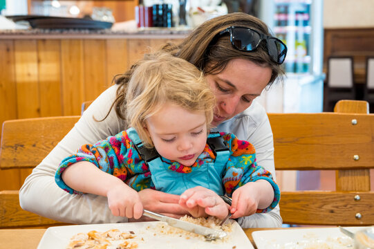 Cute blonde girl eating beef noodle soup in a restaurant with her mother.