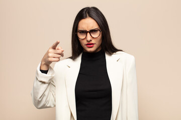 young hispanic woman pointing at camera with an angry aggressive expression looking like a furious,...