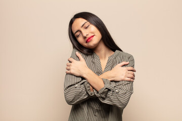 young hispanic woman feeling in love, smiling, cuddling and hugging self, staying single, being...
