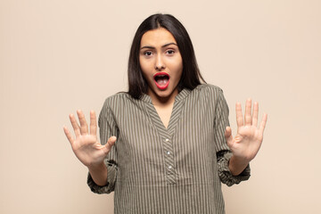 young hispanic woman feeling stupefied and scared, fearing something frightening, with hands open...