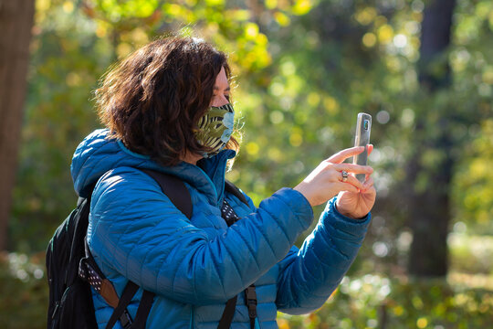Mature woman with mask looks at her mobile phone on a sunny autumn day