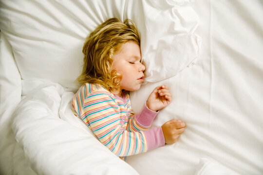 Cute Little Toddler Girl Sleeping In Big Bed Of Parents. Adorable Baby Child Dreaming In Hotel Bed On Family Vacations Or At Home.