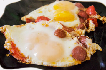 Morning roasted whole eggs on the black plate and with tomato and sausages