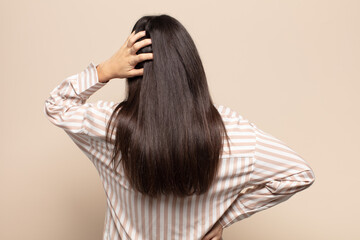 young hispanic woman feeling clueless and confused, thinking a solution, with hand on hip and other...