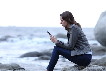 Worried woman reading phone message on the beach