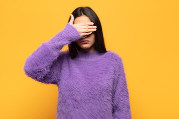 young hispanic woman covering eyes with one hand feeling scared or anxious, wondering or blindly...
