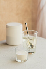 Glass with collagen dissolved in water and collagen protein powder on a light beige table. Healthy lifestyle concept.