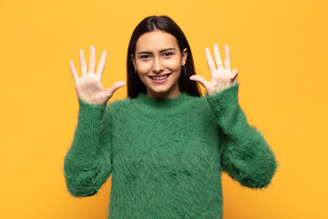 young hispanic woman smiling and looking friendly, showing number nine or ninth with hand forward,...