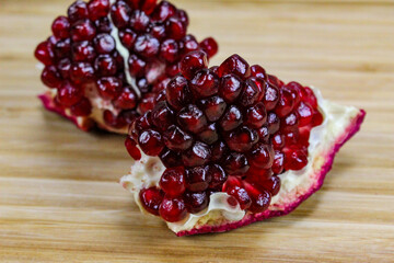 Two pieces of pomegranate with red seeds on a wooden tray. Pomegranate seeds. One piece in front and the other piece of ripe pomegranate fruit behind.