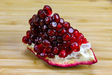 Part of a pomegranate with red seeds on a wooden tray. Pomegranate seeds. A piece of ripe pomegranate fruit.