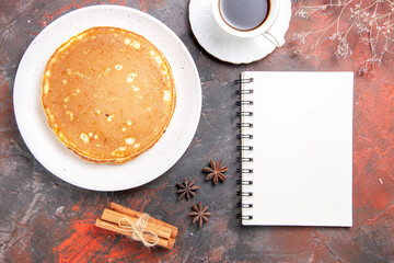 Obraz na płótnie Canvas Vertical view of homemade pancakes cinnamon lime a cup of tea and notebook on mixed color table