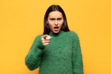 young hispanic woman pointing at camera with an angry aggressive expression looking like a furious,...