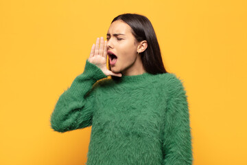 young hispanic woman yelling loudly and angrily to copy space on the side, with hand next to mouth