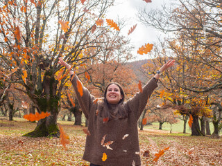 woman enjoying autumn and catching falling yellow leaves