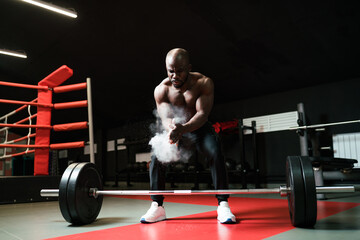 An African American man sprays magnesium or talcum powder with his palms before lifting a barbell....