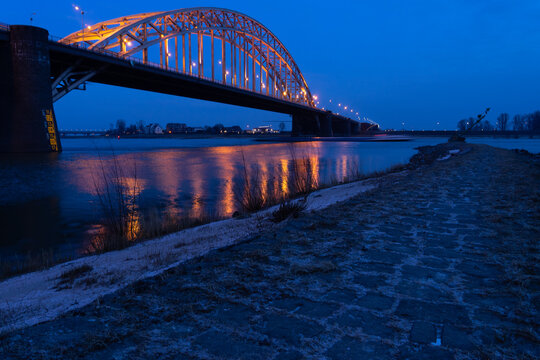 Waalbridge over the flooded river Waal at Nijmegen in wintertime at dusk with lights and a dark blue sky