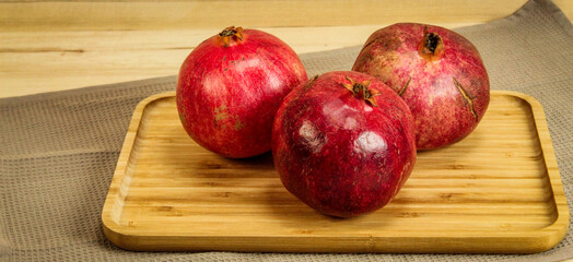 Banner. Three ripe pomegranate fruits. Red large pomegranates. Pomegranates on a wooden tray, with all the tablecloth underneath. Whole pomegranate fruit.
