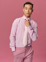 An elegant man in a pink shirt straightens his tie attractive look pink background