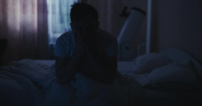 Depressed man in the bed suffers from a symptom insomnia, rubs eyes