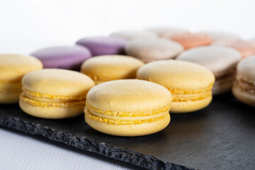 Macarons are laid out on a black slate in beautifully colored rows.