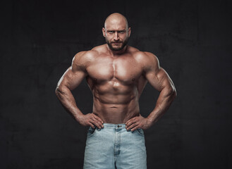 Obraz na płótnie Canvas Powerful and handsome bodybuilder with hairless head poses in dark background with naked torso with angry face looking at camera.