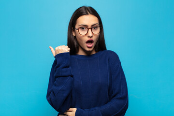 young hispanic woman looking astonished in disbelief, pointing at object on the side and saying...