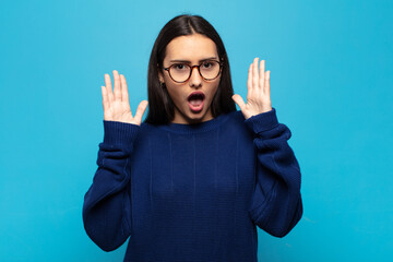 young hispanic woman looking shocked and astonished, with jaw dropped in surprise when realizing...