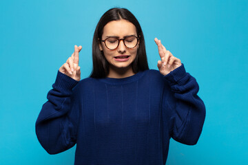 young hispanic woman crossing fingers anxiously and hoping for good luck with a worried look