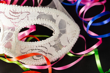 Half of a white festive carnival mask on a black background with a multi-colored serpentine.