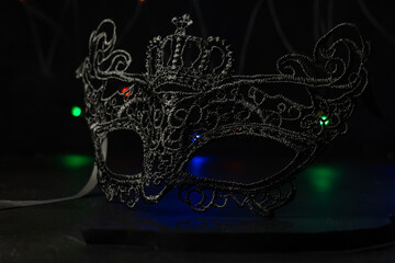 Black festive carnival mask on a black background with multi-colored garlands.