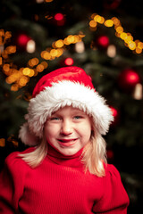 cute blond girl portrait in front of green christmas tree with fairy lights