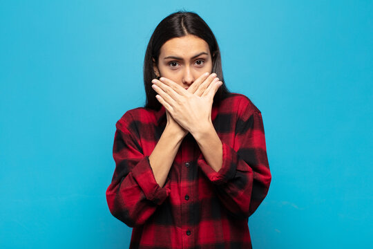 young hispanic woman covering mouth with hands with a shocked, surprised expression, keeping a secret or saying oops