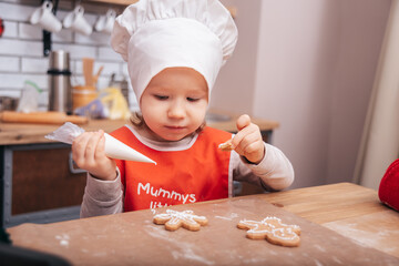 Baking holiday cookies. Child decorates Christmas cookies with icing. Seasonal Christmas lifestyle at home with children. Santa helper.