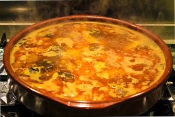 Boiling broth with meat and sausages in a clay pot