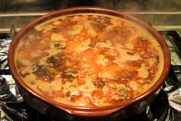 Boiling broth with meat and sausages in a clay pot