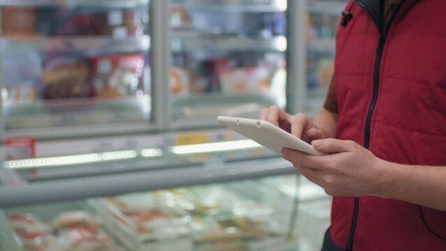 Midsection slow-motion shot of male hypermarket merchandizer walking along counters making notes in tablet