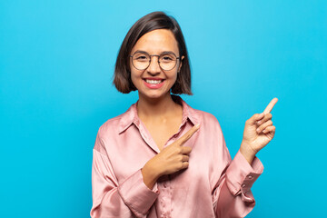 young hispanic woman smiling happily and pointing to side and upwards with both hands showing...