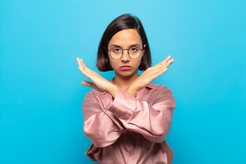 young hispanic woman looking annoyed and sick of your attitude, saying enough! hands crossed up...