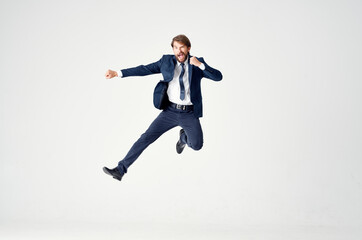 Energetic business man in a blue suit jumps up on a light background success joy emotions