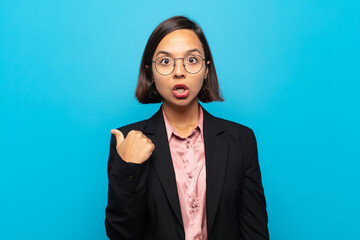 young hispanic woman looking astonished in disbelief, pointing at object on the side and saying...