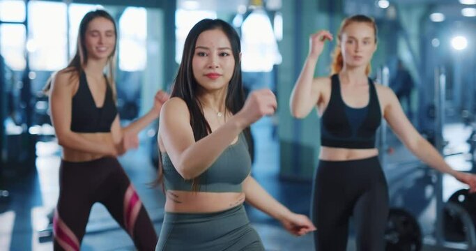 Giinger trainer young woman with girl friends doing aerobics cardio exercise together training hard in the gym. Girl power. Feminine strength. Workout.