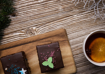 chocolate cakes and a cup of tea with orange and anise on a wooden table and branches of a Christmas tree. selective focus.