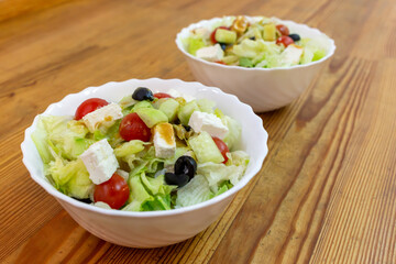 Greek salad in two white plates on a wooden surface.